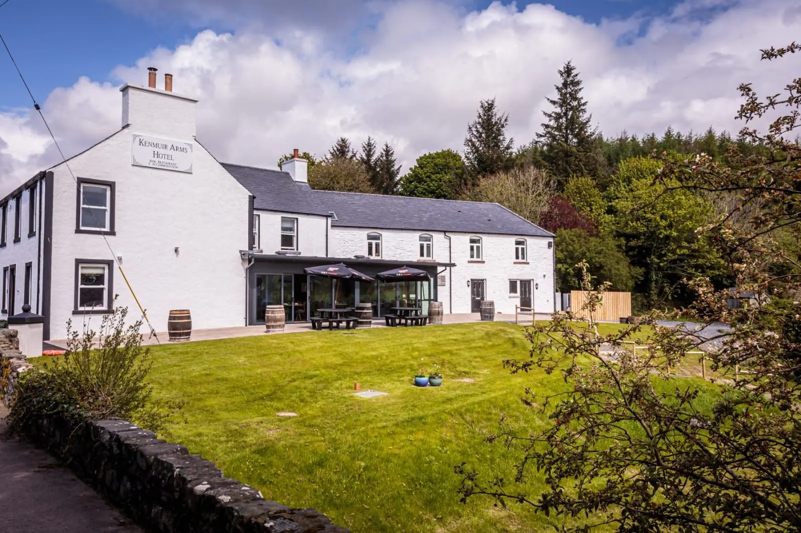 The Kenmuir Arms: a whitewashed two-storey inn with a glass-fronted restaurant, behind a lawn under a blue sky