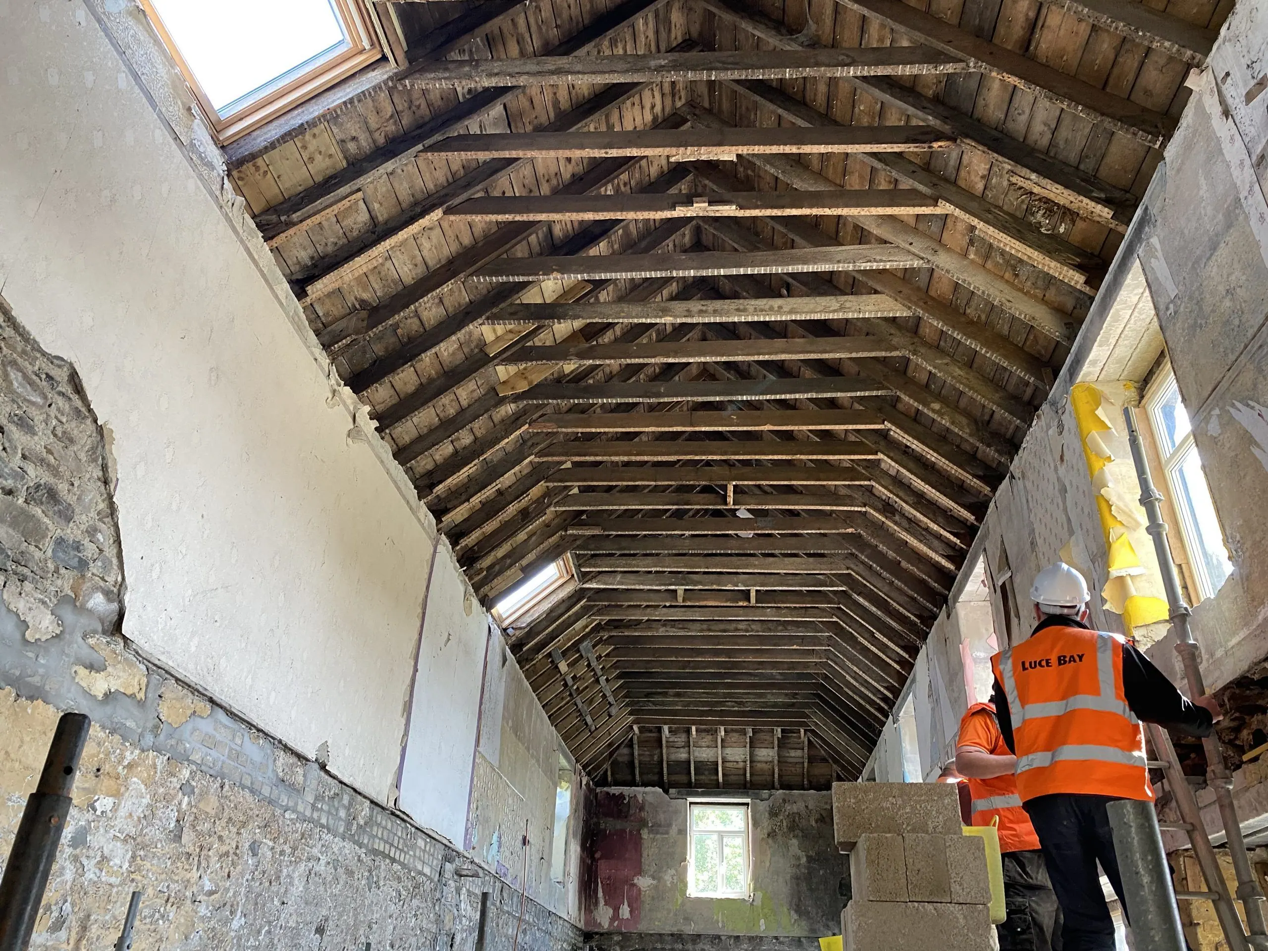 Inside the inn during the works: an open roof of old timbers above a builder in a high-visibility jacket